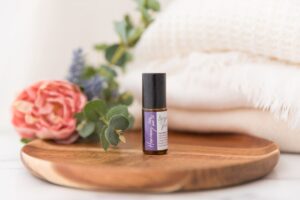 An aromatherapy pulse point oil for balance on a pretty wooden tray with foliage around it.